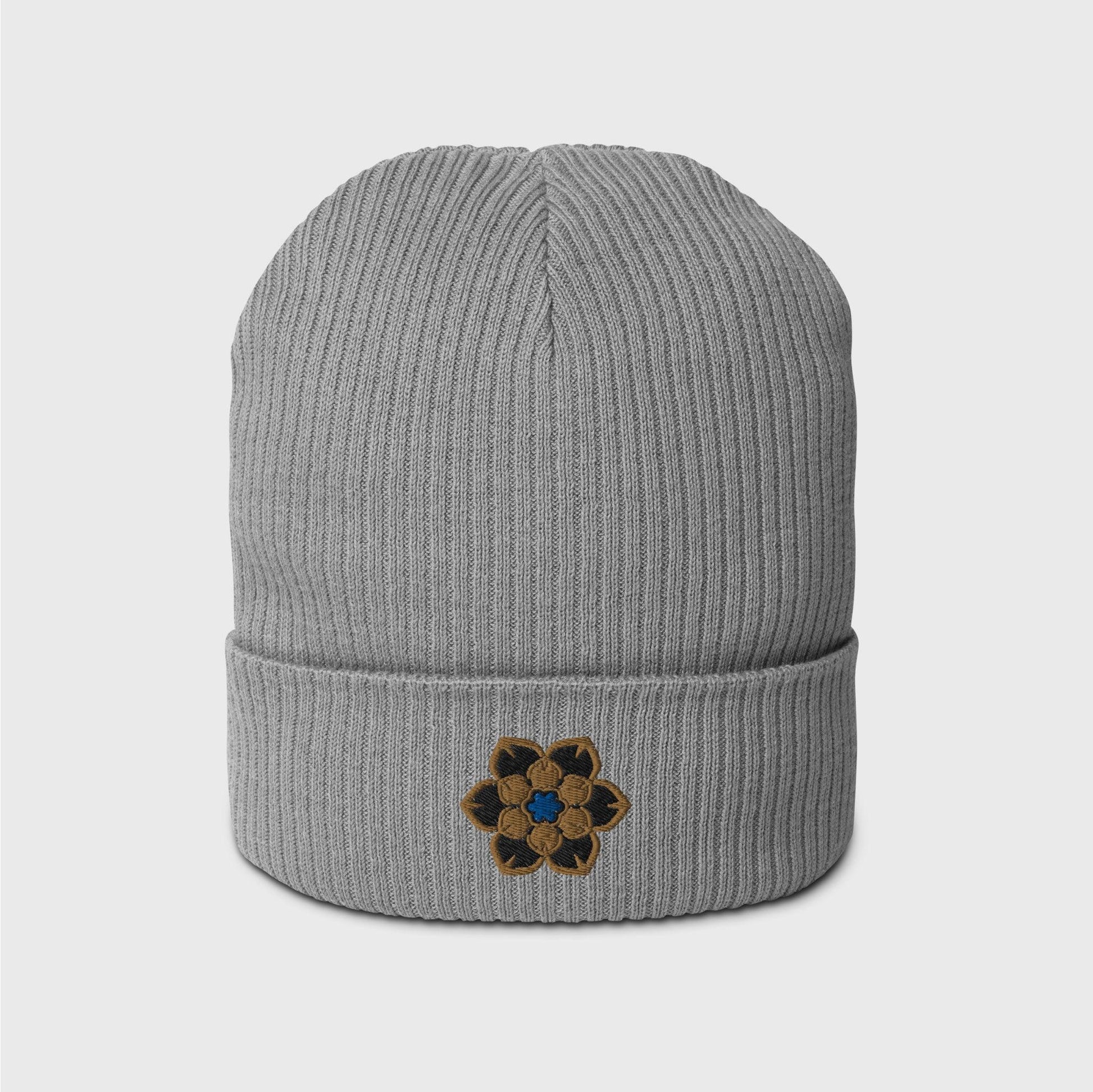  A light grey ribbed beanie featuring an embroidered logo in the shape of the Wanderer's hat, a gold 6 point hexagonal frame around a filled in black with another gold filled shaped inside and a blue figure in the centre.