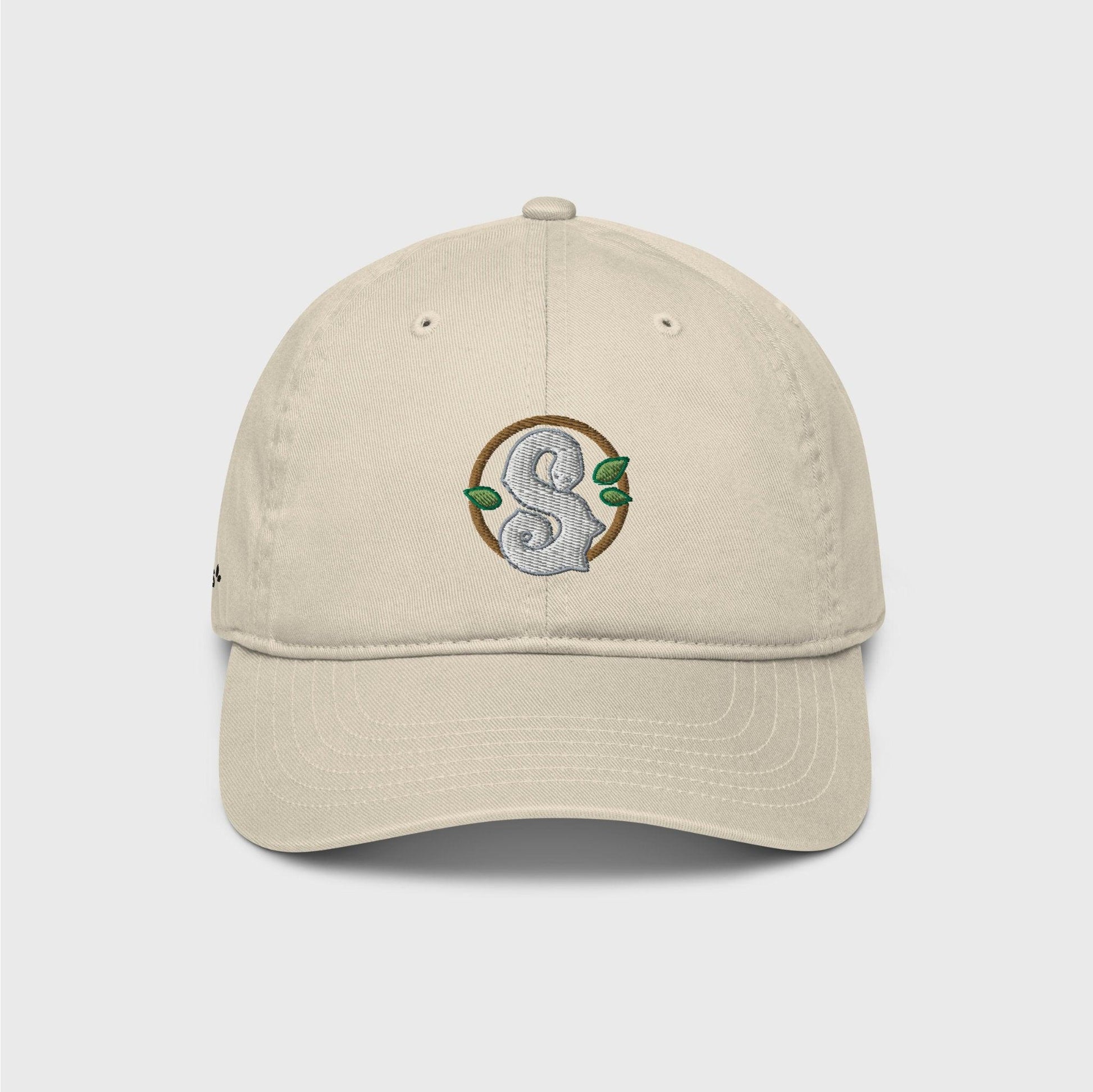 A beige classic cap featuring a round dark green frame enclosing a white snake in the shape of an S in the centre. Three small green leaves ornament the frame around the snake.