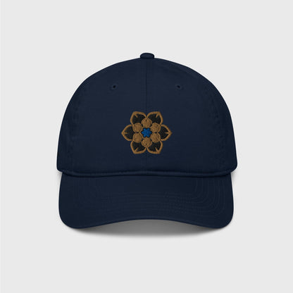 A classic blue navy cap featuring an embroidered logo in the shape of the Wanderer's hat, a gold 6 point hexagonal frame around a filled in black with another gold filled shaped inside and a blue figure in the centre.