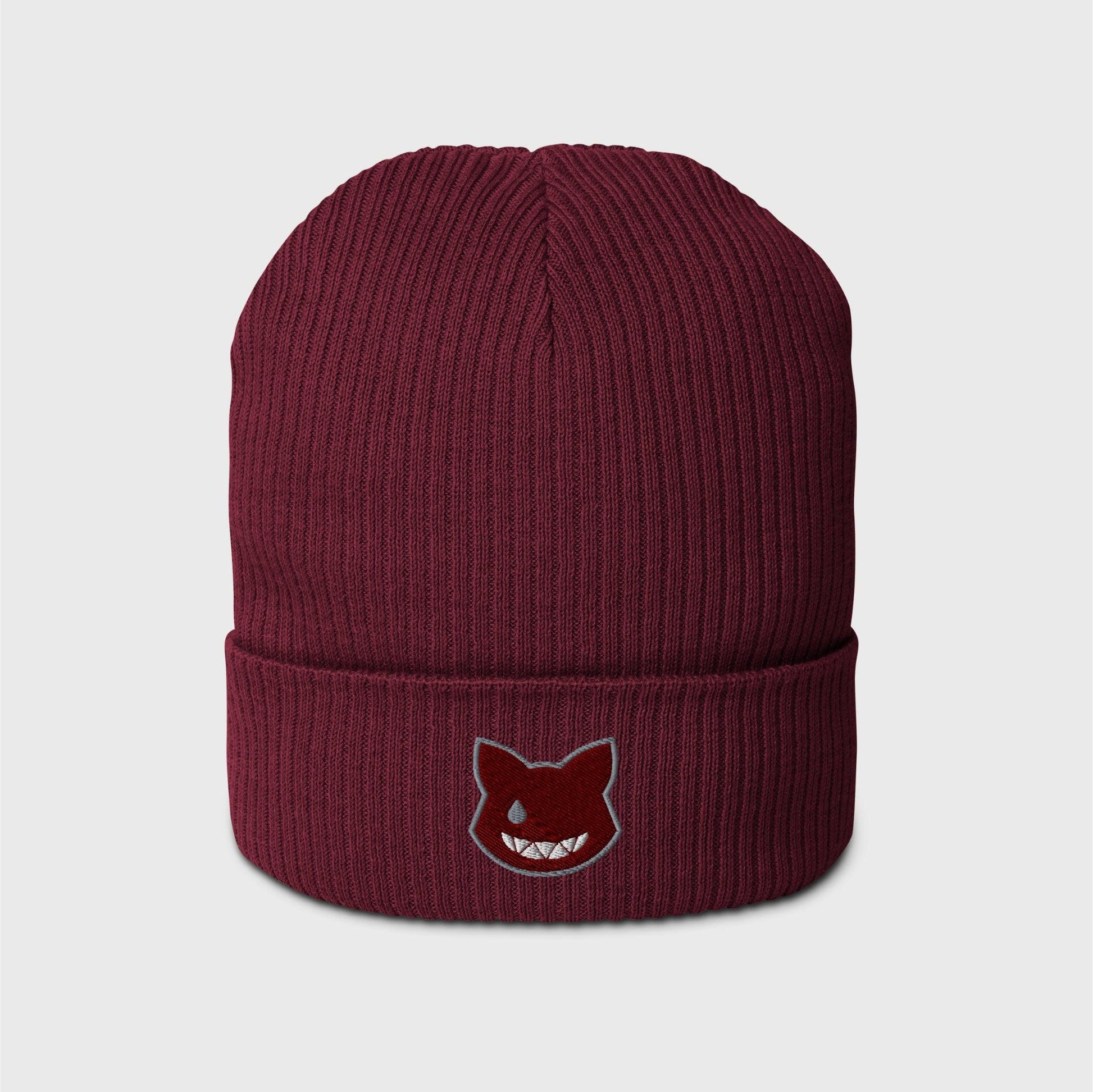 A burgundy ribbed beanie featuring an embroidered wine red logo shaped as a cat’s head, lined in grey, showing only a left grey eye the shape of a water drop and a fanged white smile.