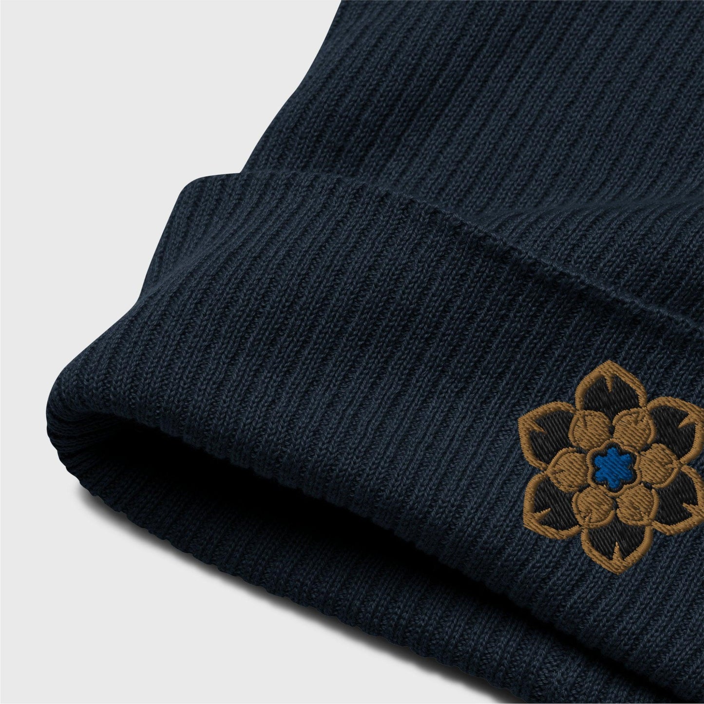 A detailed picture of the ribbed beanie showing the embroidered logo up close. you can see the organic cotton texture of the beanie folded up