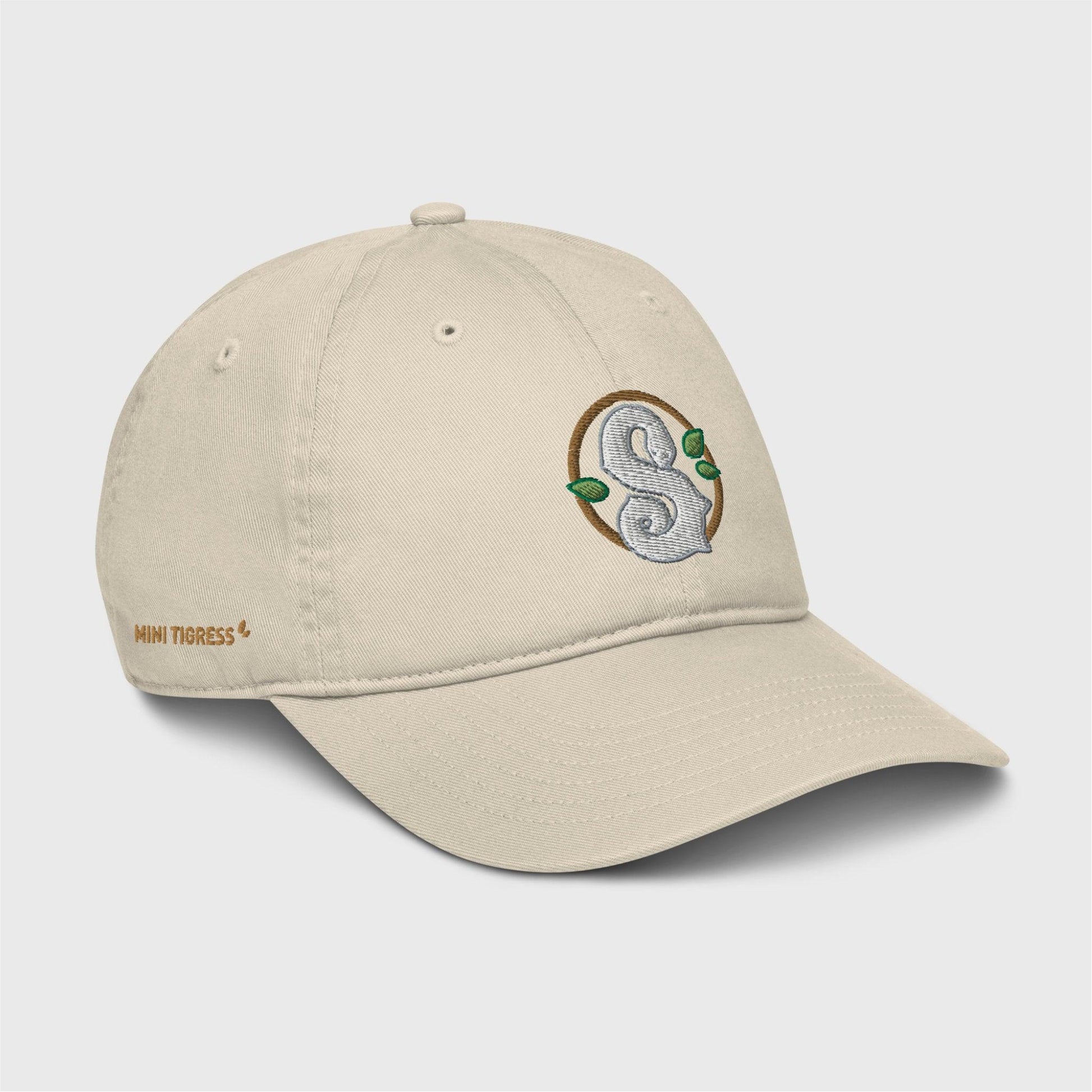 A side view of the beige cap showing the embroidered logo at the front and gold letters on the right side of the cap at the bottom saying "Mini Tigress”.