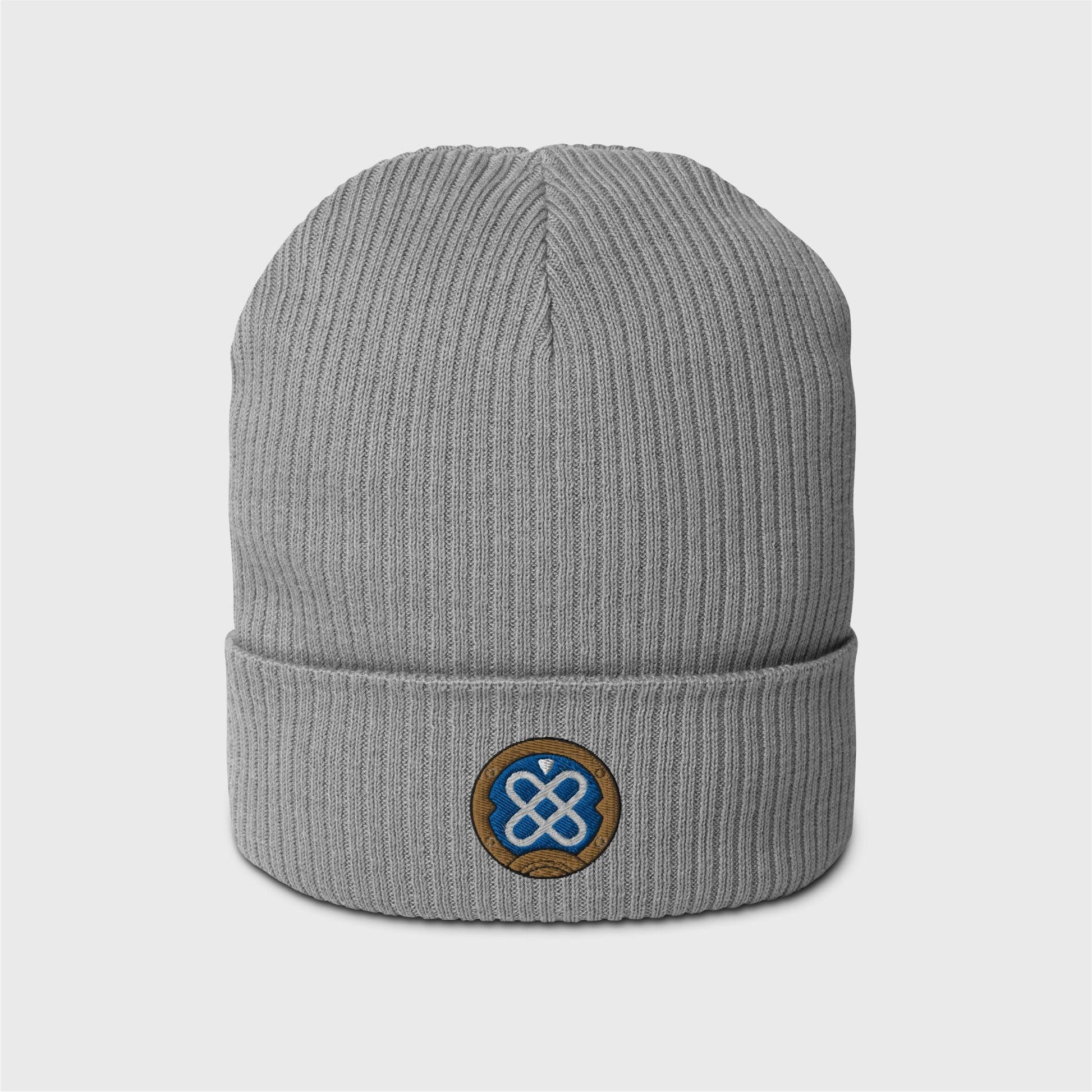 A light grey ribbed beanie featuring an embroidered round logo of Freminet's diving helmet, in blue with a white round shapes crossed in the centre and a round gold border around it.