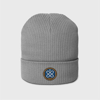 A light grey ribbed beanie featuring an embroidered round logo of Freminet's diving helmet, in blue with a white round shapes crossed in the centre and a round gold border around it.