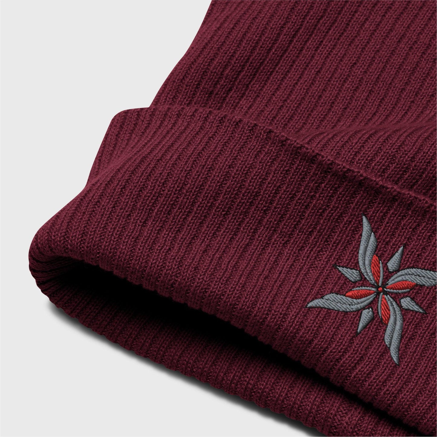 A detailed picture of the ribbed beanie showing the embroidered logo up close. you can see the organic cotton texture of the beanie folded up