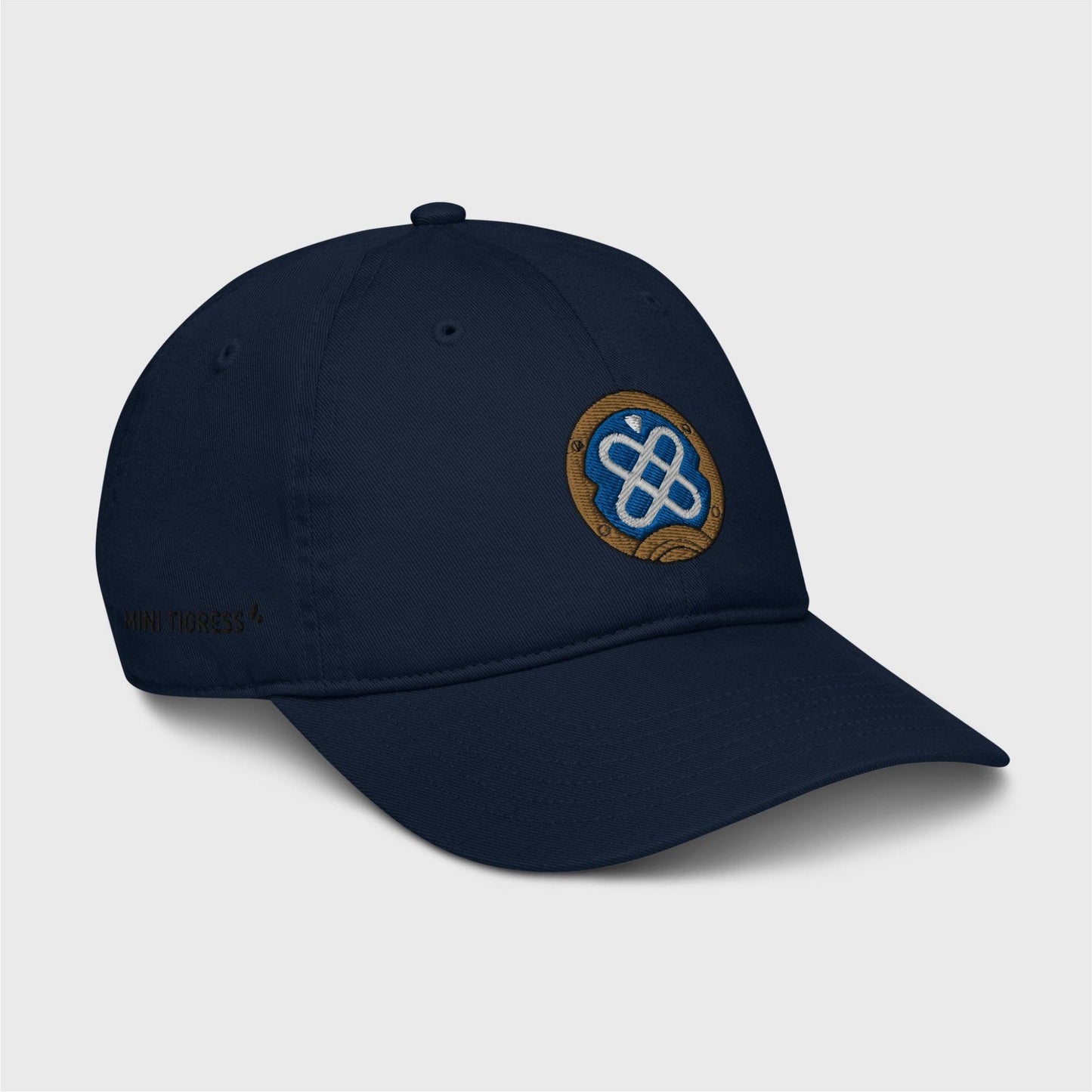 A side view of the navy blue cap showing the embroidered logo at the front and black letters on the right side of the cap at the bottom saying "Mini Tigress” barely visible.