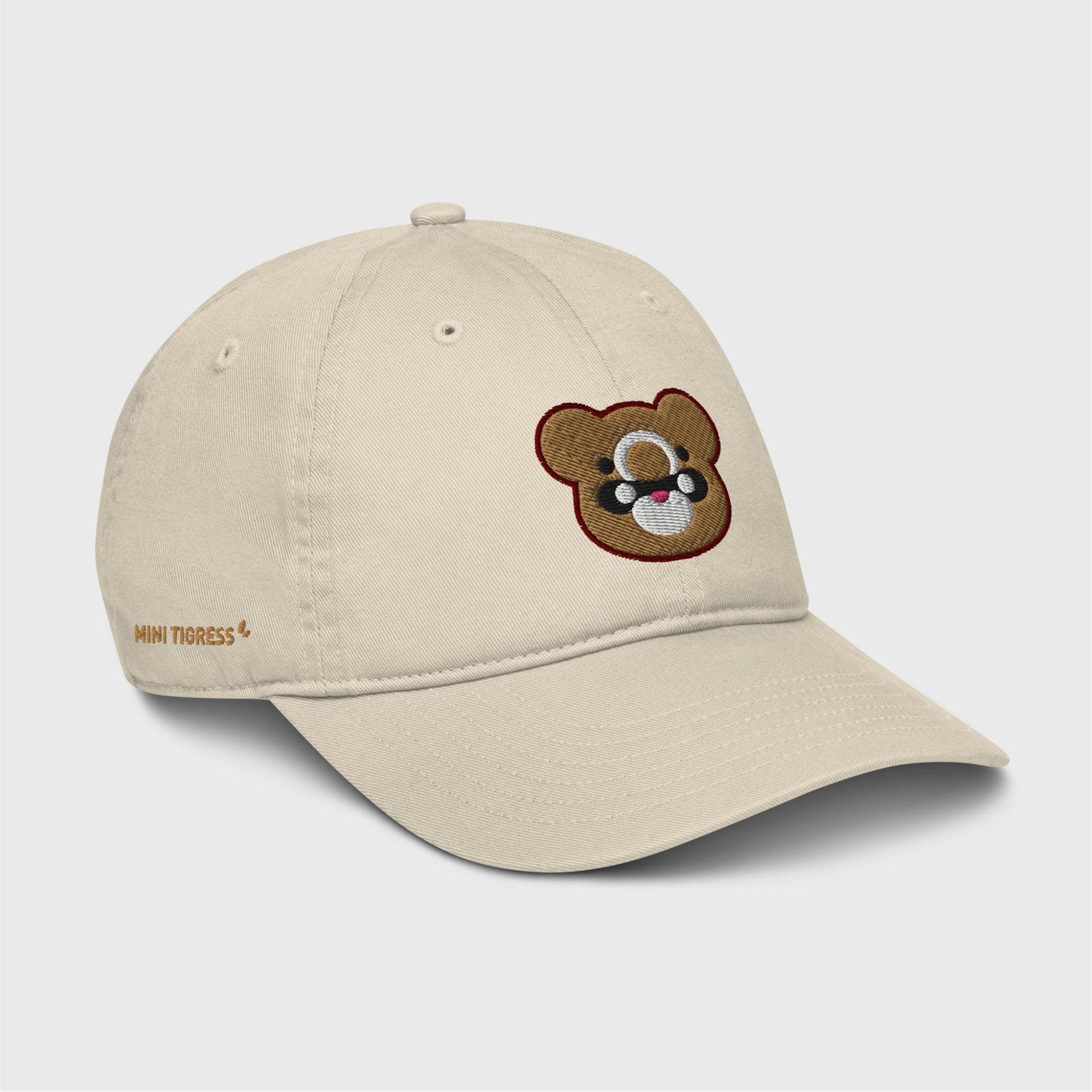 A side view of the beige cap showing the embroidered logo at the front and gold letters on the right side of the cap at the bottom saying "Mini Tigress”