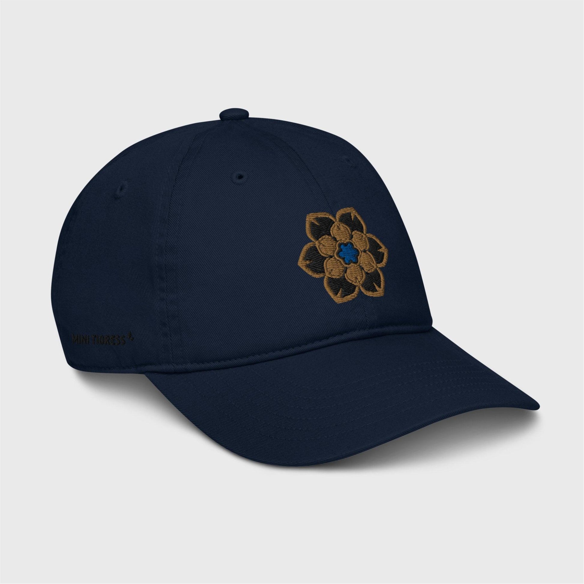 A side view of the navy blue cap showing the embroidered logo at the front and black letters on the right side of the cap at the bottom saying "Mini Tigress” barely visible.