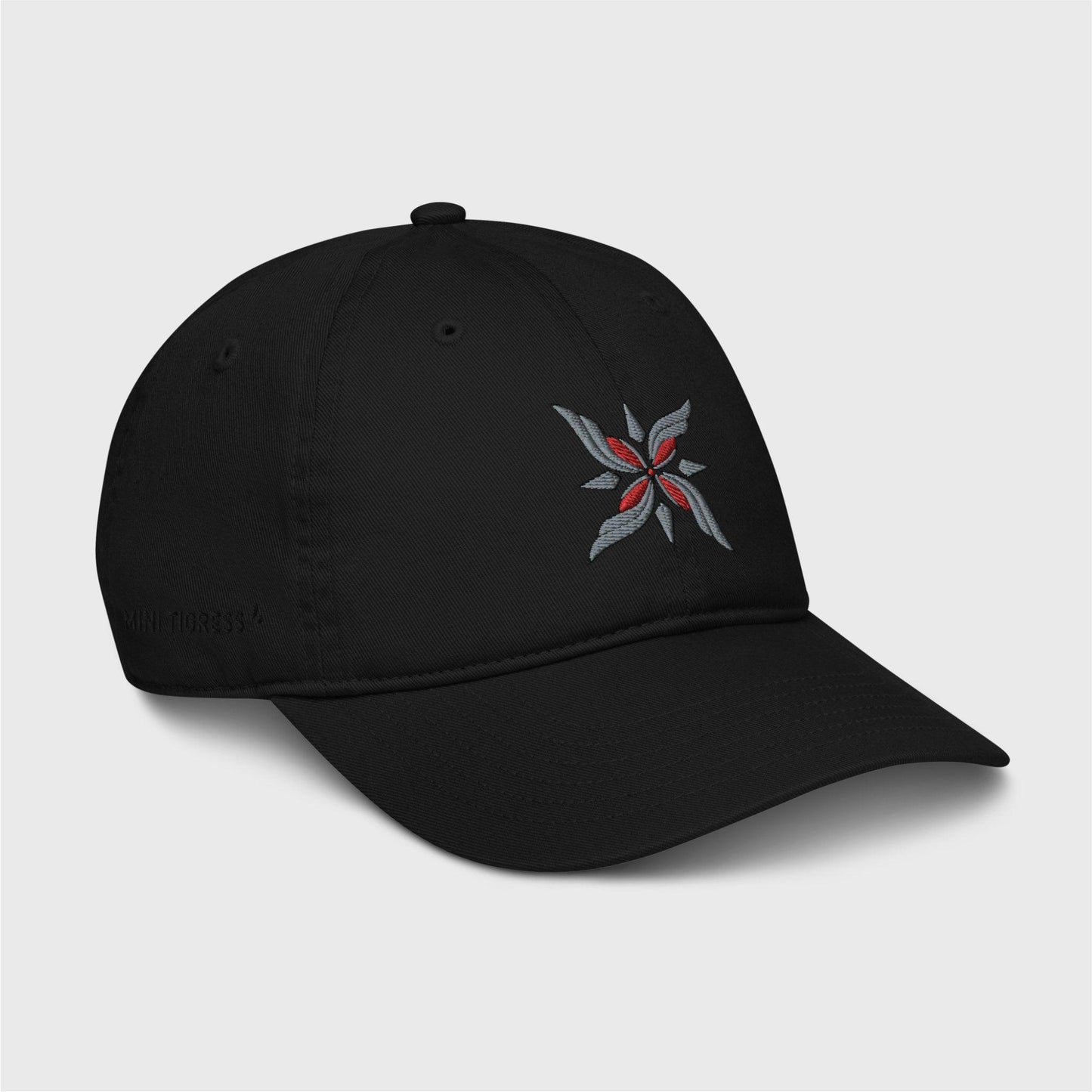 A side view of the black cap showing the embroidered logo at the front and black letters on the right side of the cap at the bottom saying "Mini Tigress” barely visible.