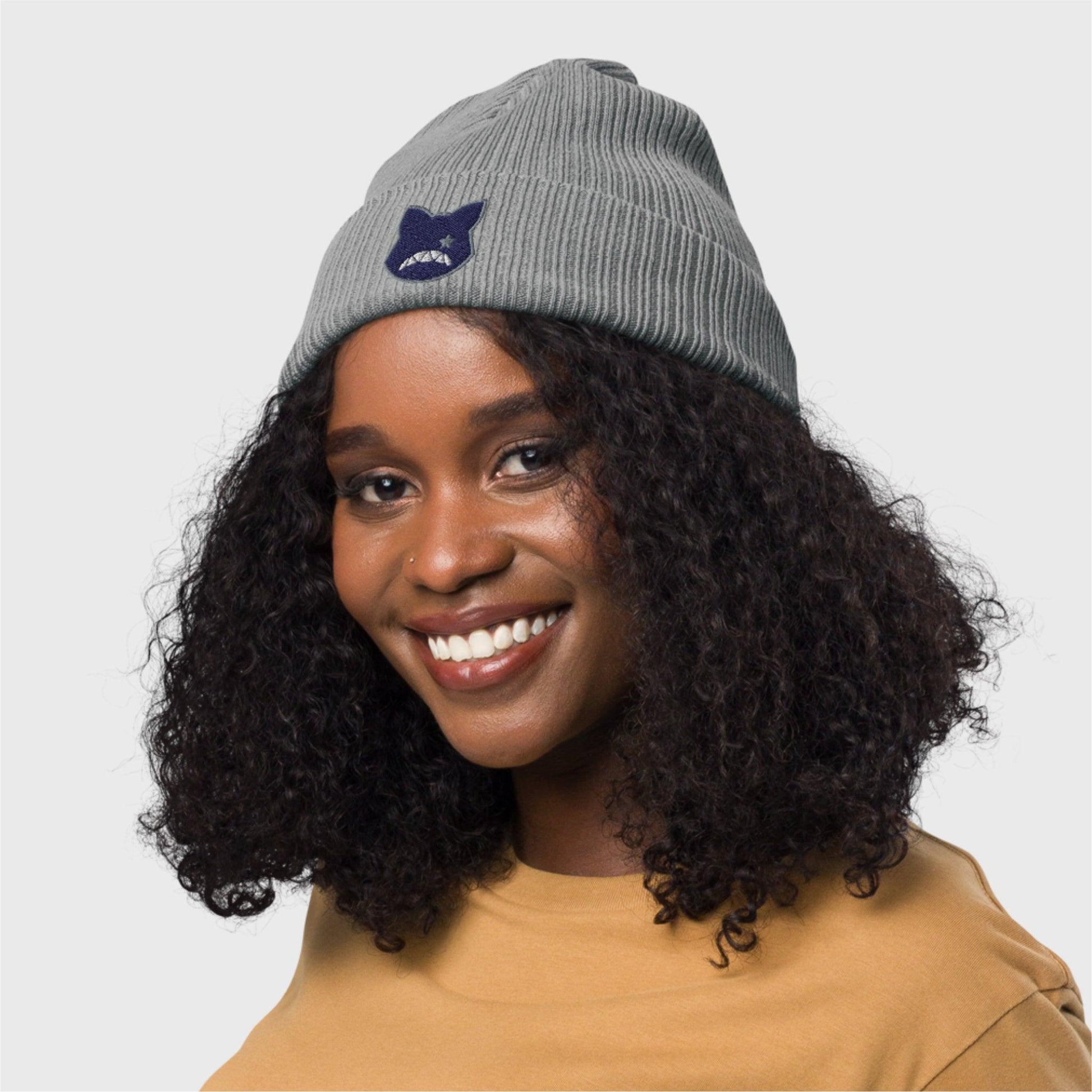 A woman smiles at the camera sideways, showing the grey beanie with the embroidered logo at the front.