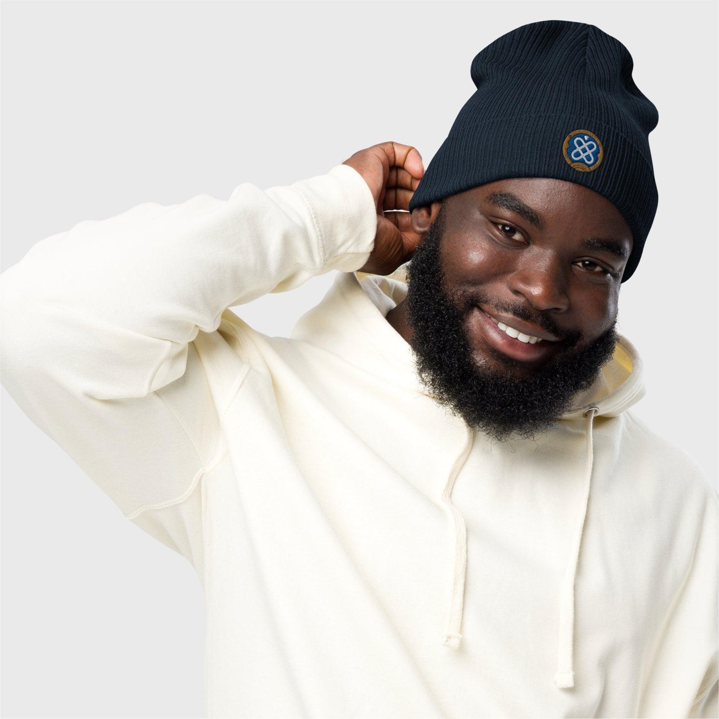 A man looks at the camera holding the back of the navy blue beanie with one hand, showing the embroidered logo at the front